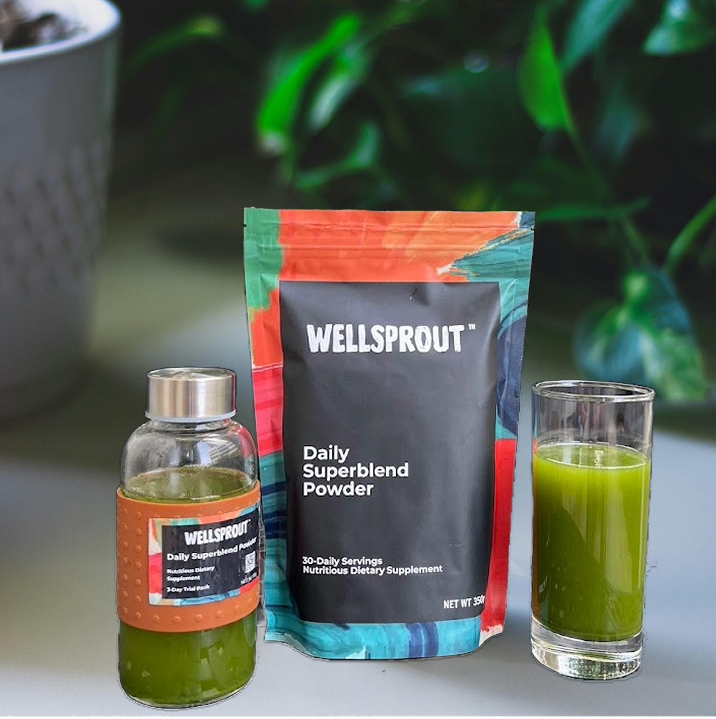 Wellsprout Daily Superblend Powder package with a bottle and glass of green juice on a blurred plant background.